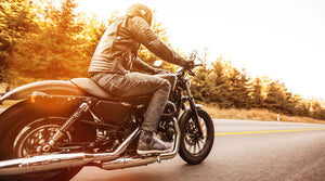 Motorcyclists riding a motorbike with trees in the background and the sunsetting