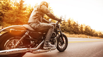 Motorcyclists riding a motorbike with trees in the background and the sunsetting