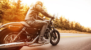 Motorcyclists riding a motorbike with trees in the background and the sunsetting