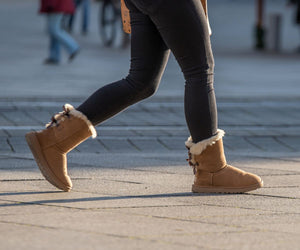 Person walking outdoors in tan sheepskin ankle boots.