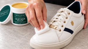 Gently applying Renapur Leather Balsam to a white leather trainer with a white application sponge.