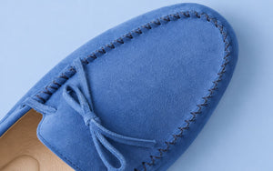 Close-up of a blue suede loafer showing its soft nap, stitched edging and bow detail.