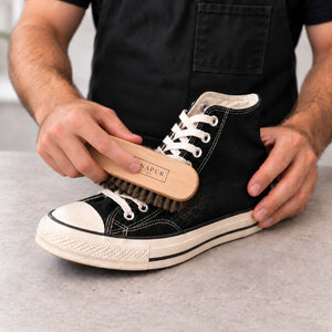 Brushing loose dirt from a black canvas trainer with a Renapur Horsehair Brush.