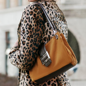 Woman in a leopard-print coat carrying a tan suede shoulder bag.