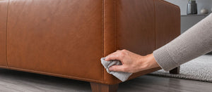 Patch testing leather cleaner with a soft cloth on a small area at the lower back of a brown leather sofa.