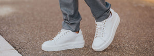 Person wearing white-coloured leather trainers on a stone pavement.