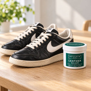Renapur Leather Balsam beside black and white leather trainers on a pale wooden table at home.