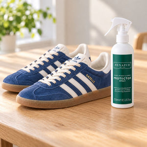 Renapur Suede & Fabric Protector beside blue suede trainers with white stripes on a pale wooden table at home.