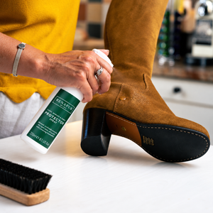 Renapur Suede & Fabric Protector beside blue suede trainers with white stripes on a wooden table.