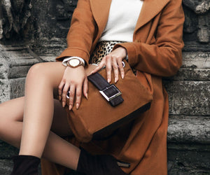 Woman holding a tan suede handbag with dark leather trim.