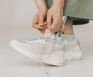 Person tying the laces of white trainers with mesh panels.